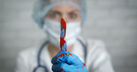 Steel scalpel in blood. A scared doctor in protective uniform hold a medical tool in blood in hand.