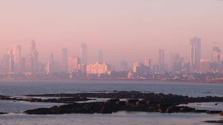 Real time wide angle view of Mumbai City Skyline as seen from famous tourist destination Marine Drive during golden hour. Wide shot of buildings during pink sunset. Bombay, Maharashtra, India.