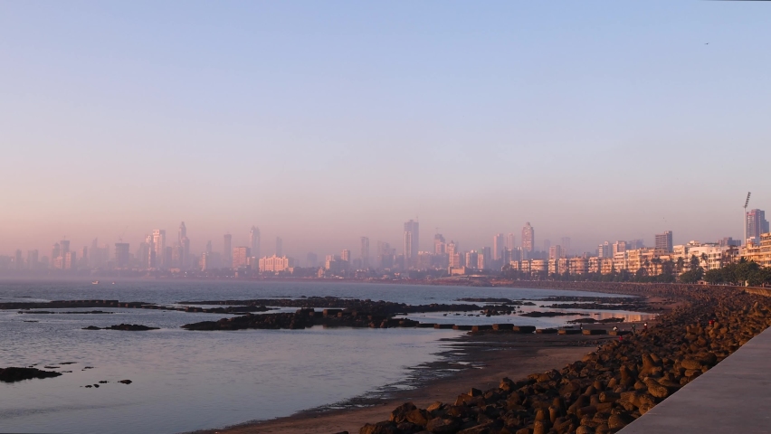 Real time wide angle view of Mumbai City Skyline as seen from famous tourist destination Marine Drive during golden hour. Wide shot of buildings during pink sunset. Bombay, Maharashtra, India.