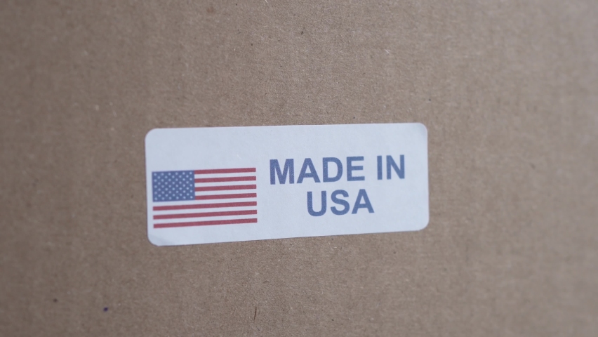 Hands applying MADE IN USA label on a shipping cardboard box with products inside. Closeup shot.