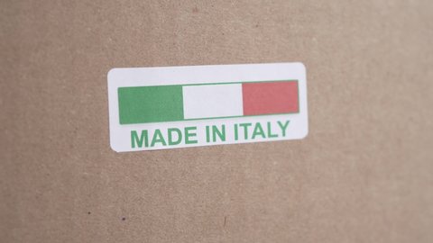 Hands applying MADE IN ITALY label on a shipping cardboard box with products inside. Closeup shot. Label with flag