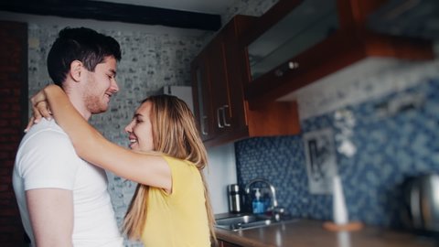 Young preety couple kissing passionately in the kitchen. Sexy young girl is in light clothing with her handsome man are spending time together, hugging. Concept of love, family, passion.