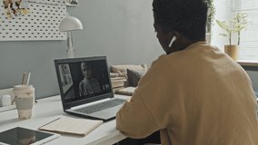 African American man in wireless earphones sitting at desk and talking with woman in hijab via video call while having online lesson at home