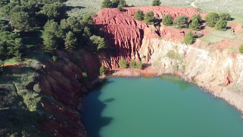 Otranto 2022. Aerial top-down view from a drone flying over the canyon between mountains of iron-red soil that are reflected in the green waters of the lake of the bauxite quarry