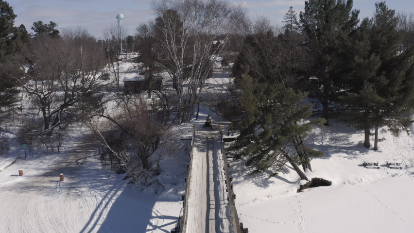 Group of snowmobiles rides on wooden overpass bridge above frozen lake in northern Wisconsin.  Winter adventure, aerial view