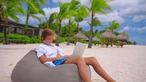 Boy at online lesson with tutor. Kid use laptop against the background of the turquoise water. Young boy attending an online lesson during the lockdown
