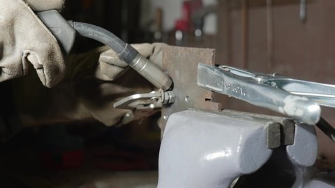 Welding of two metals with gloves and welding helmet in vice grip
