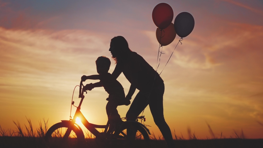 mom teaches son to ride a bike. happy family kid dream concept. mom and child son learn to ride a bike silhouette in the park in nature. sunlight happy family doing sports outdoors in the park . Royalty-Free Stock Footage #1087645820