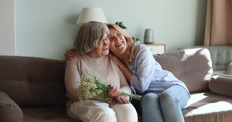 Loving middle-aged female congratulates 80s mom with birthday. Older woman get chamomile flowers from relative sit on sofa enjoy family holiday. Life event, love, Happy Mother Day celebration concept Royalty-Free Stock Footage #1087646075