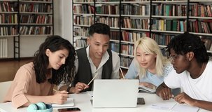 Four diverse teammates students study remotely using pc in scientific library discuss task make notes in workbooks. Motivated young people of some ethnic groups doing high school assignment together