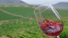 Waving red wine in a glass on defocused vineyard background . Beautiful stock footage for wine commercial . Close up video of wine mixing process inside goblet . Shot on ARRI ALEXA in Slow Motion .