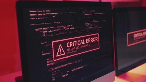 Tracking out of critical error warning message showing on computer screen on desk in office in dark, red light flashing