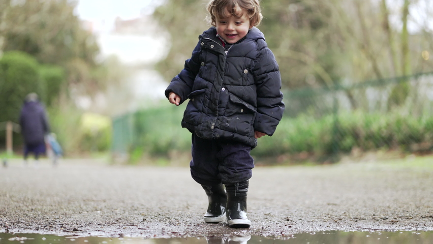 Little baby boy jumping into water puddle and running in mud water wearing boot rains Royalty-Free Stock Footage #1087655384