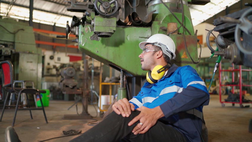Man labor worker had accident and sit beside cutting equipment at the production line of CNC machine factory. Engineer man help and support him on injured. Safety in industrial factory. Injury at work