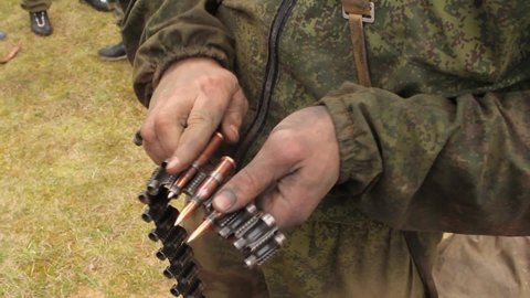 Inserts large-caliber bullets into the machine-gun belt. Close up. Lots of cartridges and ammunition. One soldier feeds the second one