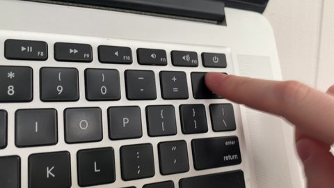 Fair skinned female repeatedly presses delete backspace button on her laptop while typing regrettable comments on social media group forums from her professional office email account