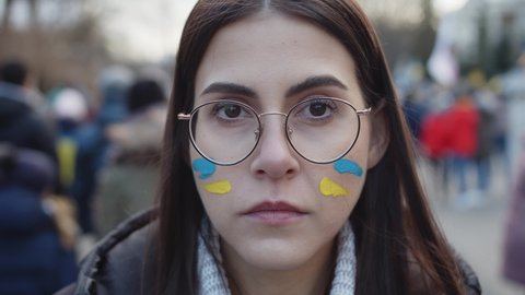 WARSAW, POLAND - FEBRUARY 27 2022: Close Up Portrait Girl With The Flag Of Ukraine On Face, Stands On Demonstration, Protest Against The Russian War Invasion In Ukraine. Ukrainian Flag, Protesters