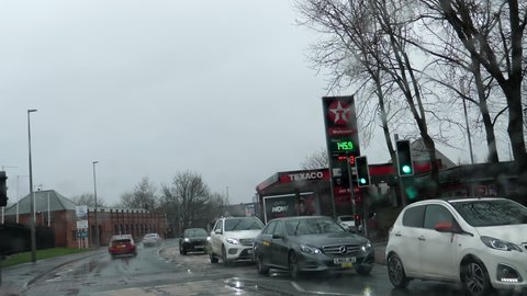 SALFORD, GREATER MANCHESTER, ENGLAND, UNITED KINGDOM - CIRCA FEBRUARY, 2022: Car point of view, POV driving in Lower Broughton in rain past petrol station or gas station Texaco, crossing river Irwell.