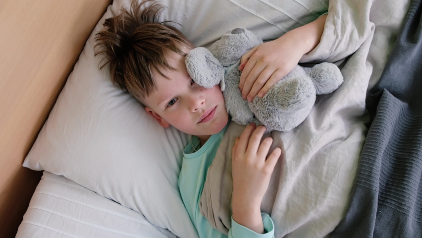 A sad boy lies on the bed with a fever and headache and rubs his head in pain. The face is twisted with pain | Shutterstock HD Video #1087669013