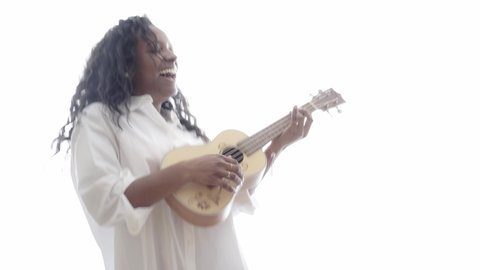 Isolated Woman playing Ukelele standing in white background. Beautiful Latin girl comfortable at home enjoying cheerful music. Concept of leisure and relaxation.