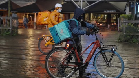 Ghent , Belgium - 02 18 2022: Deliveroo Delivery Rider Wearing Thermal Backpack and Winter Uniform Getting on his bike and Rides on the City Center Road To Deliver Orders for Clients and Customers - S