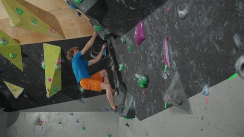 Slow motion, young climber training on a climbing wall, man practicing rock-climbing and moving up.