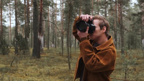 A young blond photographer takes pictures in the woods. Photographer in nature. 