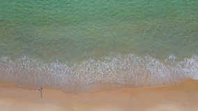 Aerial view of turquoise ocean wave reaching the coastline with tourist walking by. Beautiful tropical beach from top view. Andaman sea in Thailand. Summer holiday vacation concept. 4K drone video