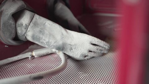 Protective rubber gloves and blasting gun in a sandblasting cabinet.