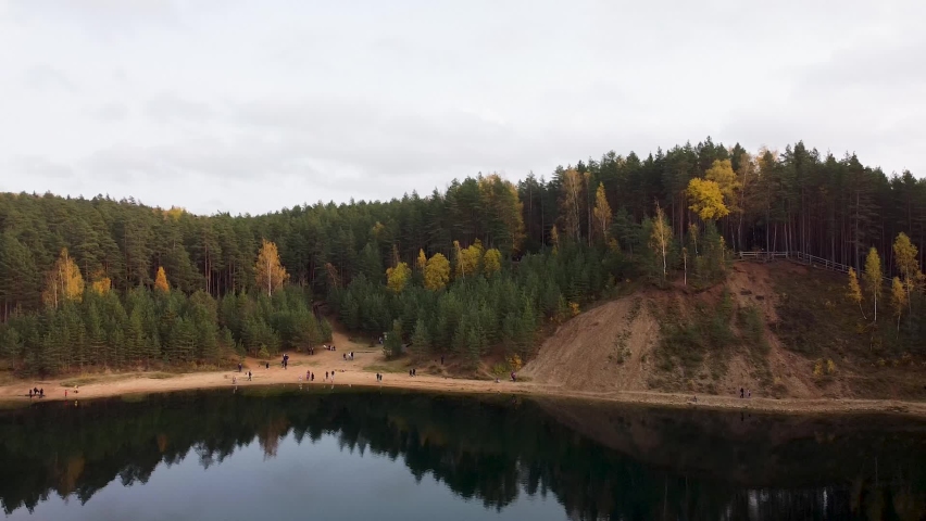 Aerial drone view of a colourful autumn forest next to a lake with sandy banks. Recorded in Ogres Zilie Kalni National Park in Latvia in Europe.