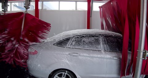 Silver car being clean by automatic brush and car wash soap in automatic car wash machine