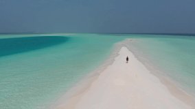 Drone following caucasian man from behind walking over picturesque sandbank, Maldives, Alif Alif Atoll, Indian Ocean. Aerial video footage of paradise, white sand, turquoise green water, blue sky.