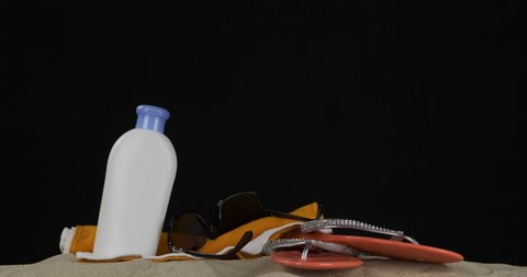 Panorama of beach accessories. Sunglasses, beach flip-flops, cream lying on the sand. Isolated on black background