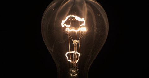 Glass light bulb and smoke from a burning spiral on a black background. The spiral of a light bulb is smoking inside a glass bulb. Close-up
