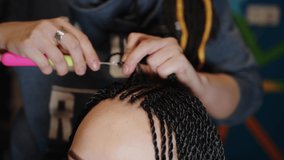 A female stylist attaches Senegalese braids to a woman in a beauty salon. Portrait of a beautiful lady with Senegalese pigtails in casual clothes. A hipster girl gets her hair done