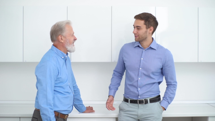 Handsome young man talking with presumed elderly father before genetic paternity test at medical clinic. Confident cheerful adult manager and smiling colleague having fun conversation in office.