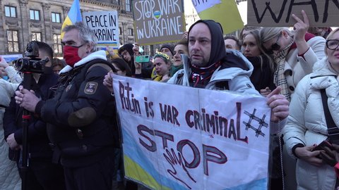 AMSTERDAM, NETHERLANDS – FEBRUARY 27 2022: Man holds sign calling Putin a war criminal, during solidarity protest with Ukraine (against Russian invasion of the country) in Amsterdam