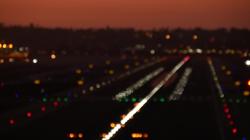 Defocused airport runway lights at night, plane or airplane taking off from airstrip, twilight dusk after sunset. Aircraft or airliner jet departure from aerodrome, San Diego airfield, California USA Royalty-Free Stock Footage #1087698797