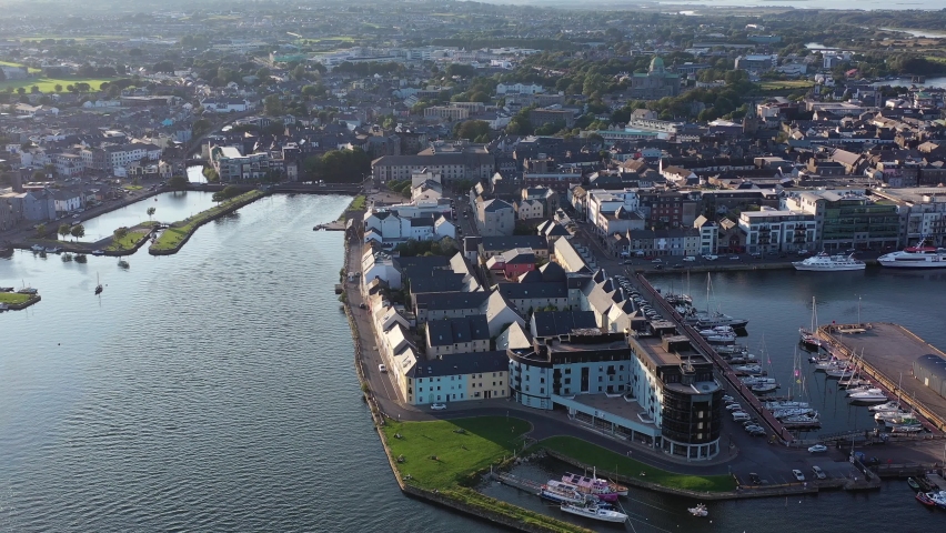 Ireland’s city of Galway in daytime as it sits by the Sea. A drone shot panning left around the dock area, showcasing the houses, busy roads and ships that are docked right beside the city.