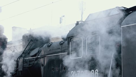 Vintage black steam locomotive. Historic train runs through fields. Vehicle departs from railway station. Old steam train locomotive is leaving the railway station.