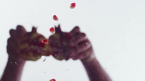 A man's hand is opening a pomegranate. Grain falling on the camera. Pomegranate seed