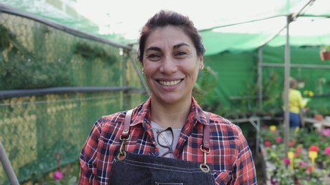 Happy Hispanic woman gardener smiling front of camera while working in flower garden shop