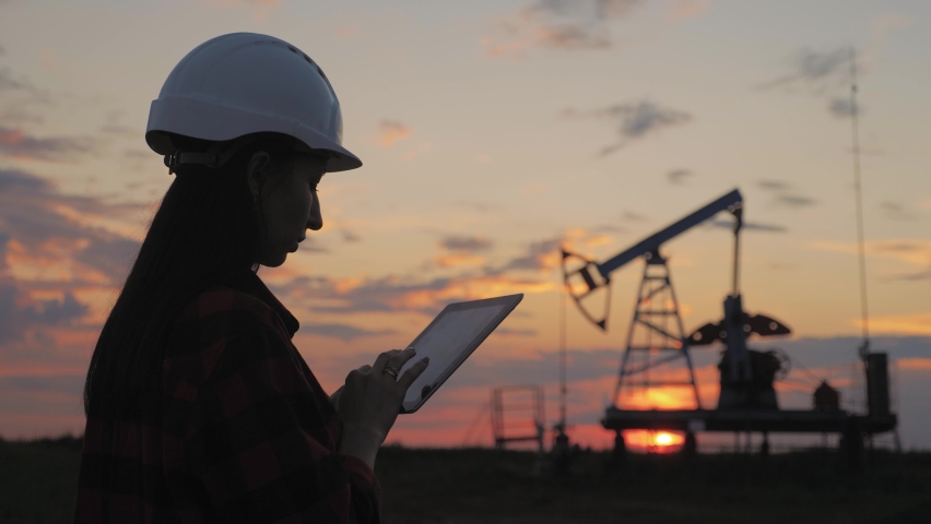 Industrial, oil and gas concept. Silhouette working engineer oil rig. Oil rigs at sunset. Silhouette of woman engineer with tablet overseeing the site of crude oil production at sunset.
