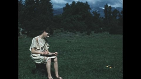 1950s: Youth in toga sits in meadow and writes.