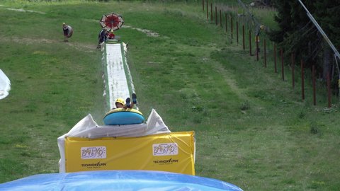 Bansko, Bulgaria 23 Aug, 2021: Summer tubing slide takes children down the hill and jump at inflatable baloon bed