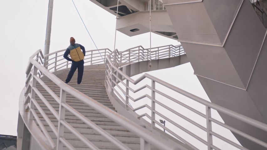 Wide slowmo of African-American man in warm activewear warming up and practicing boxing punches standing on stairs outdoors on cold morning