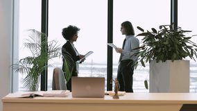 Two businesspeople discussing business or document and standing in modern office spbi. 4k video Young businesswoman, businessman look at papers in hands and talk with smiles, do work together and