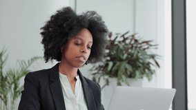 Young businesswoman working with device and posing for camera at table in modern office spbi. 4k video Portrait of attractive African female looks at computer screen and does work or browses web