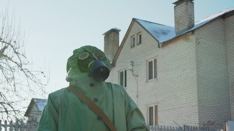 man in protective cloak and hazmat stands in village raising his head watching sky in anticipation of chemical attack from air