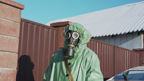 employee of organization for bacteriological and nuclear safety walking near red fence in rural area protecting his body and respiratory organs with protective equipment